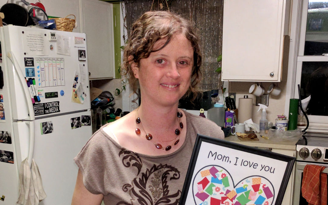 Photo of Serra holding the "I love you to pieces" art that her two and a half year old son made for her at daycare
